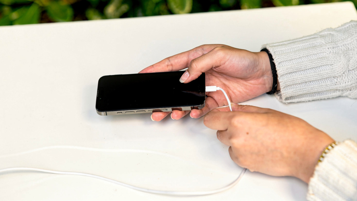 A woman plugs her smartphone charge limit at a desk, illustrating modern technology usage.